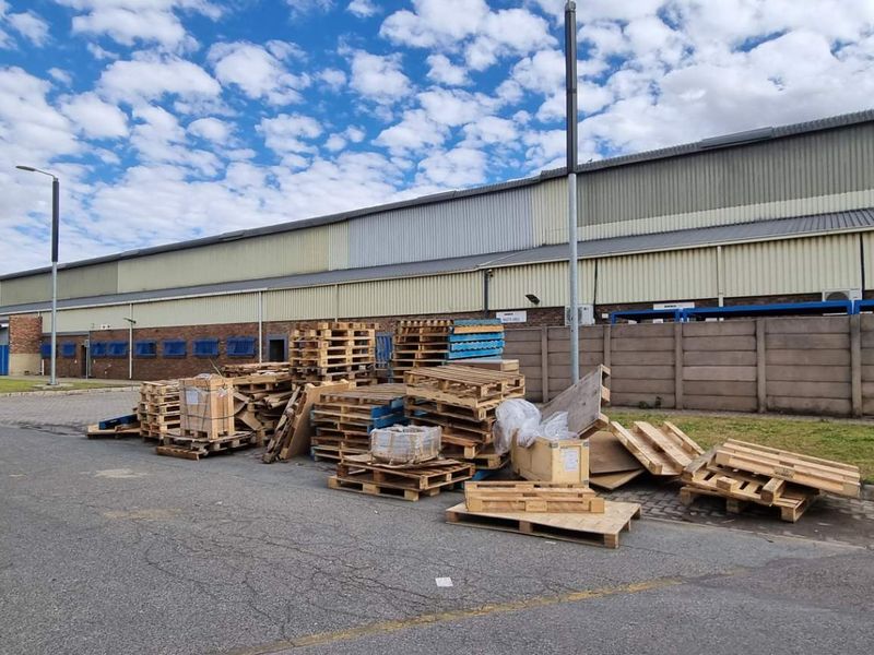 Exterior view of a commercial warehouse facility featuring a large paved yard area, perimeter wall, and metal cladding structure.