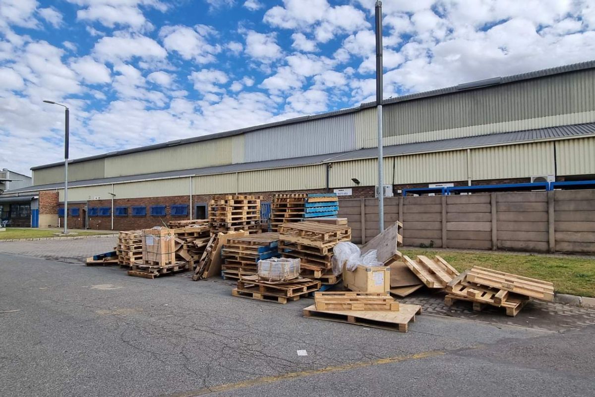 Exterior view of a commercial warehouse facility featuring a large paved yard area, perimeter wall, and metal cladding structure.