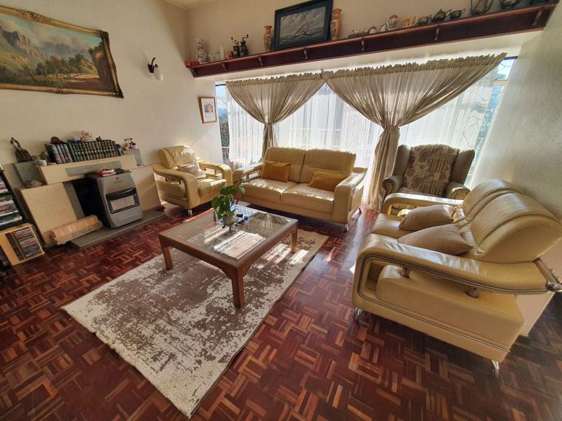 A cozy living room featuring classic parquet flooring, a built-in fireplace with a mantelpiece, and a large window allowing for natural light.