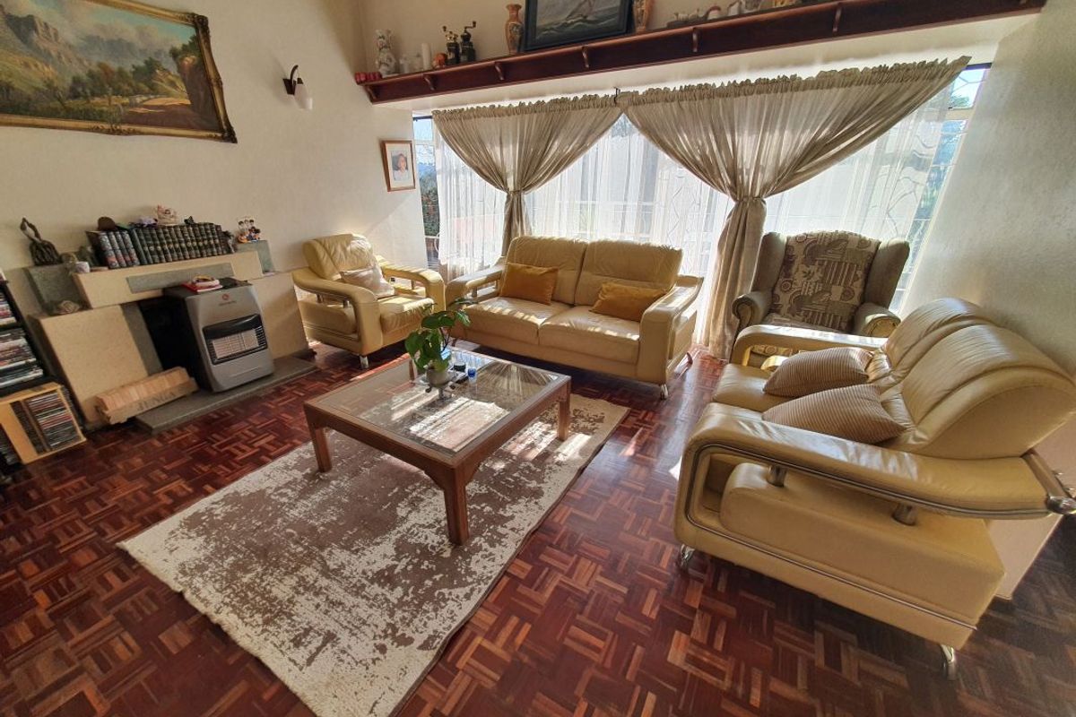 A cozy living room featuring classic parquet flooring, a built-in fireplace with a mantelpiece, and a large window allowing for natural light.