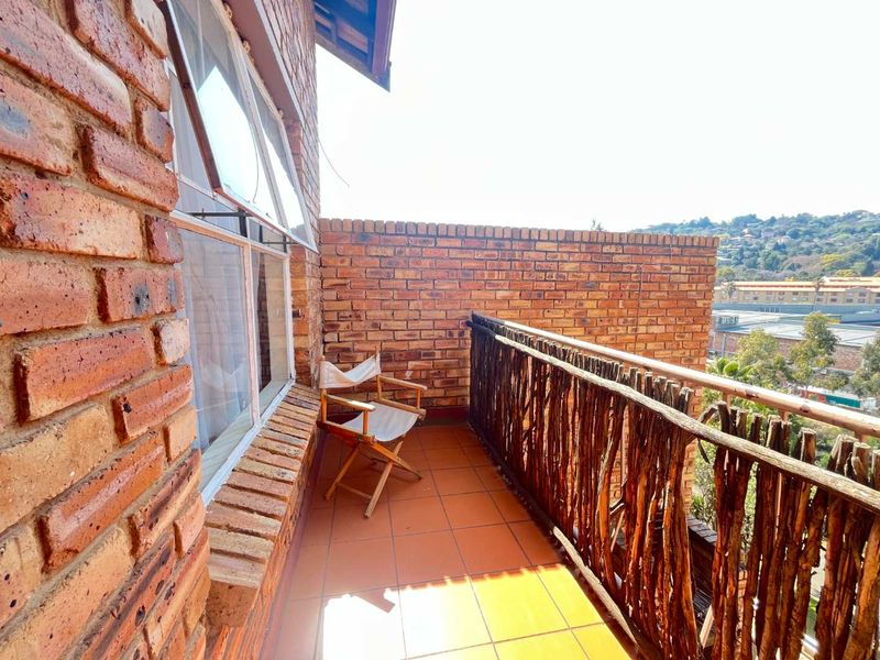 A private balcony featuring exposed brick walls, tiled flooring, and a rustic timber balustrade with views of the surrounding area.