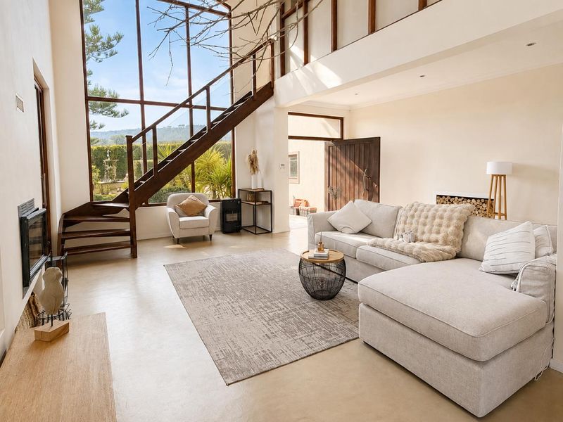 Spacious double-volume living area featuring floor-to-ceiling windows, a striking timber staircase, polished concrete floors, and a built-in fireplace.