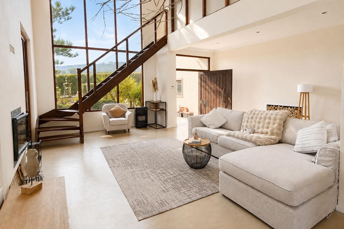 Spacious double-volume living area featuring floor-to-ceiling windows, a striking timber staircase, polished concrete floors, and a built-in fireplace.