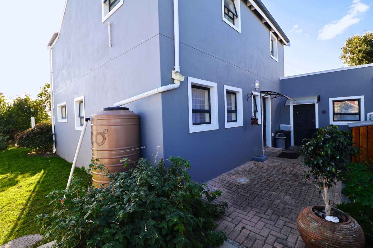 Rear exterior view of the house featuring a paved patio area, downpipe system, and a water storage tank.
