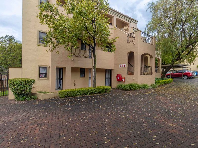 Exterior view of a multi-story apartment complex featuring paved driveway access, wrought iron balcony railings, and established landscaping.