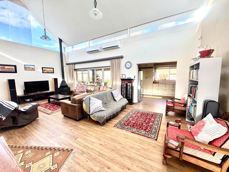 Spacious open-plan living area featuring high vaulted ceilings, clerestory windows for natural light, a wood-burning fireplace, and direct access to the outdoor patio.