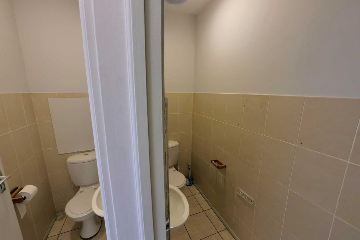 A functional office restroom featuring a toilet, wall-mounted basin, and neutral tiled walls.