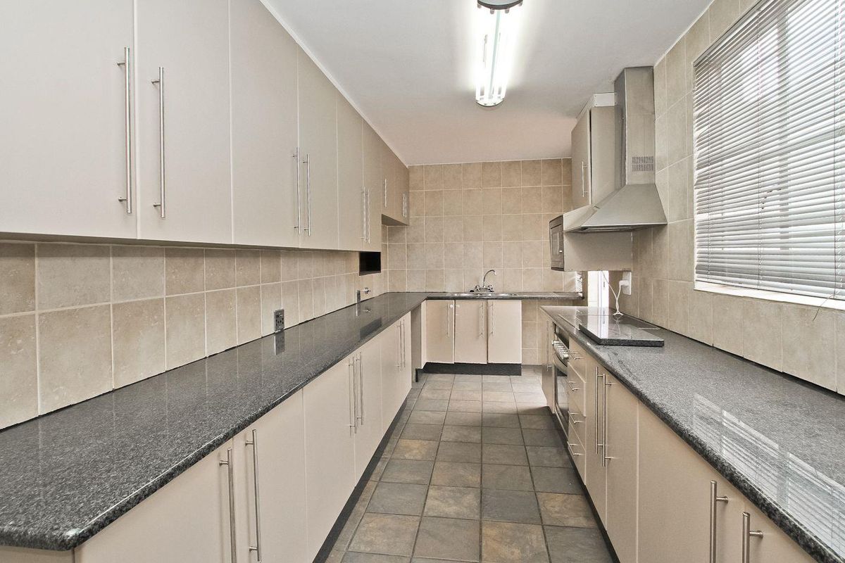 A functional galley-style kitchen featuring granite countertops, ample built-in cabinetry, a stainless steel extractor fan, and a built-in oven with a ceramic hob.