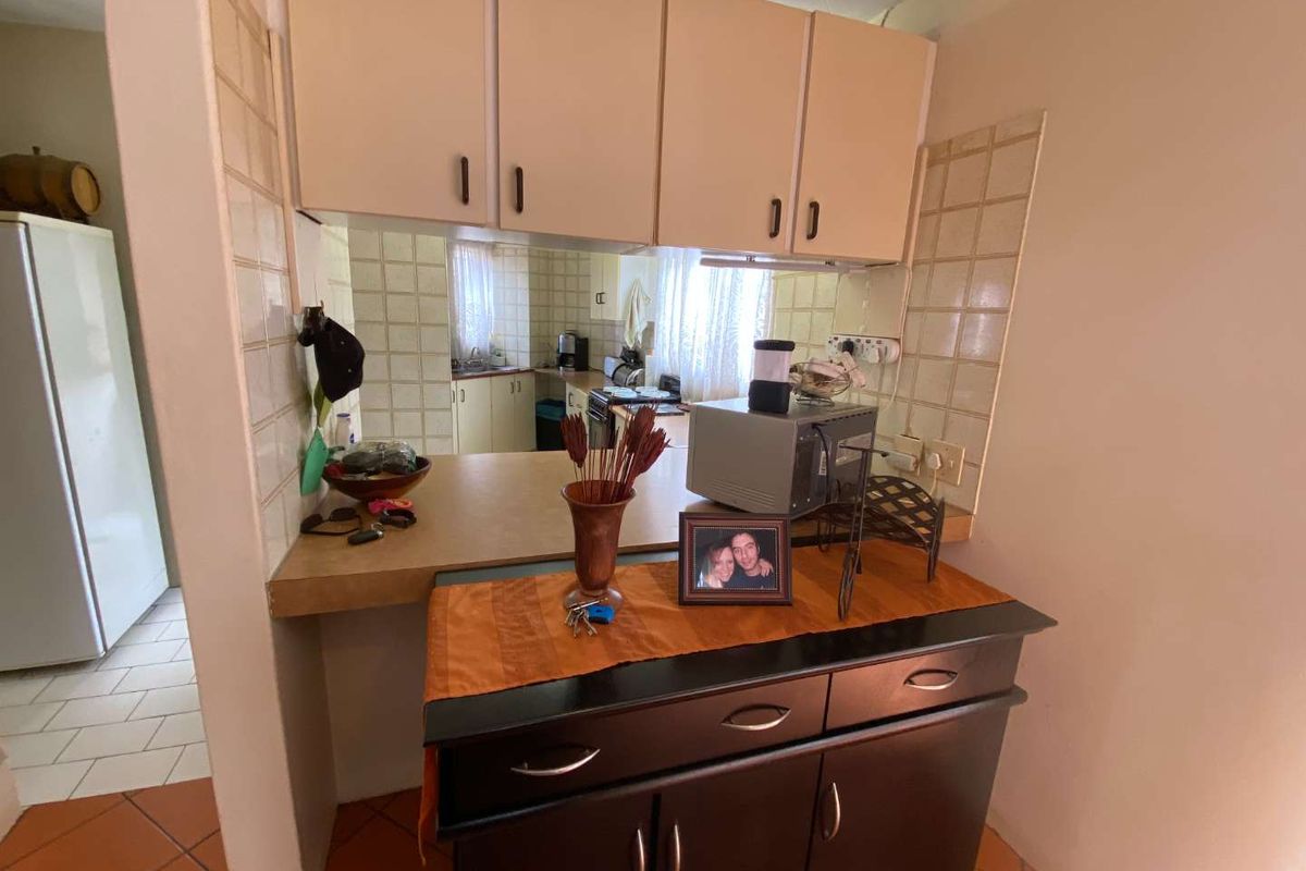 A functional kitchen featuring a breakfast bar pass-through, overhead cabinetry, and tiled backsplash, connecting to the adjacent living area.