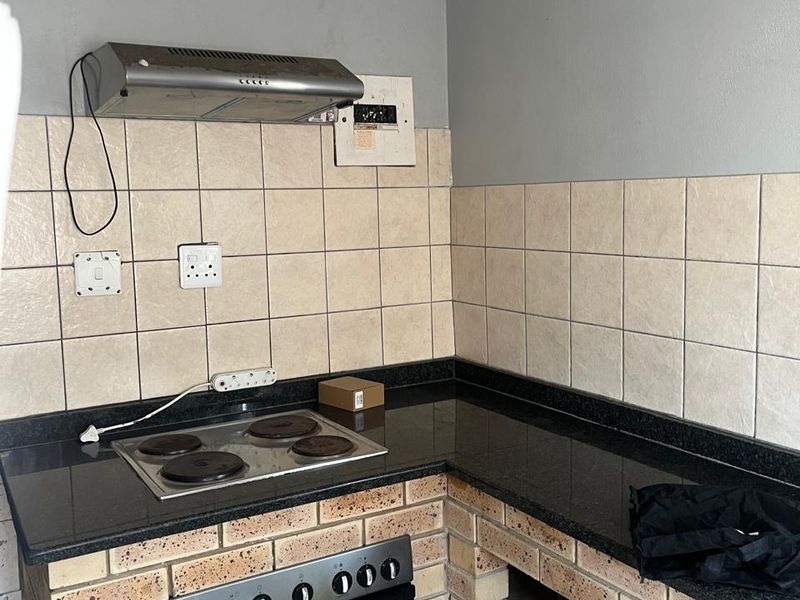 A compact kitchen featuring granite countertops, brick-based cabinetry, a built-in oven, and an electric hob with an extractor fan.
