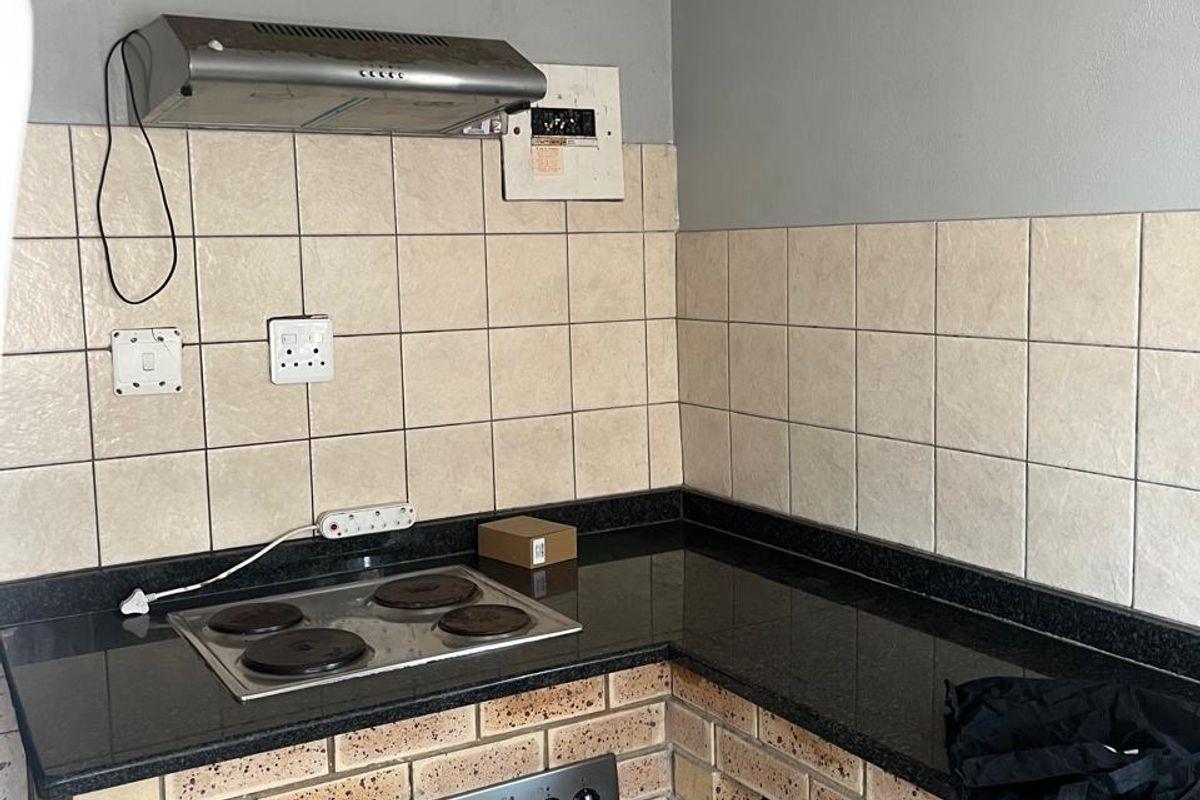 A compact kitchen featuring granite countertops, brick-based cabinetry, a built-in oven, and an electric hob with an extractor fan.