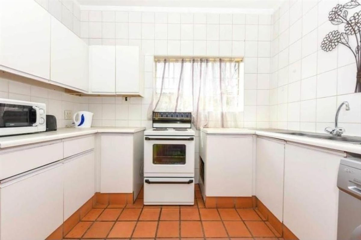 A functional kitchen featuring white cabinetry, a tiled splashback, a freestanding stove, and terracotta floor tiles.
