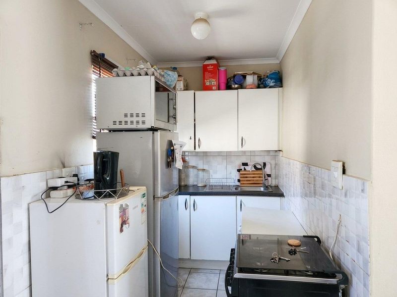 A compact kitchen featuring white cabinetry, tiled splashbacks, and tiled flooring, providing a functional workspace with essential built-in fixtures.