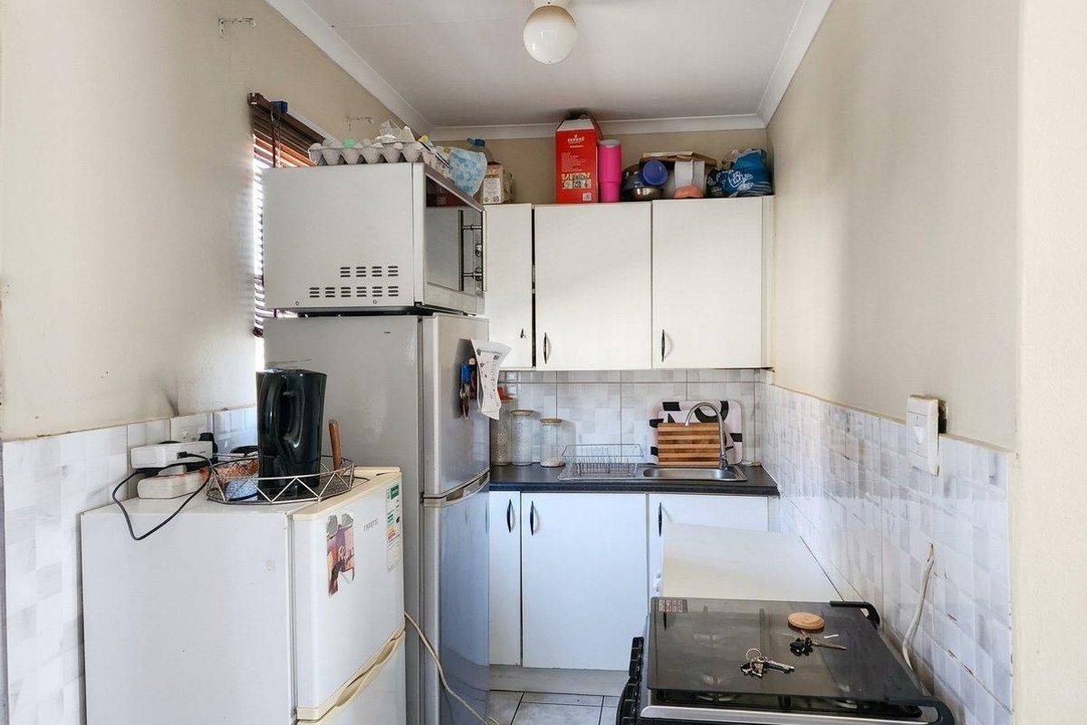 A compact kitchen featuring white cabinetry, tiled splashbacks, and tiled flooring, providing a functional workspace with essential built-in fixtures.