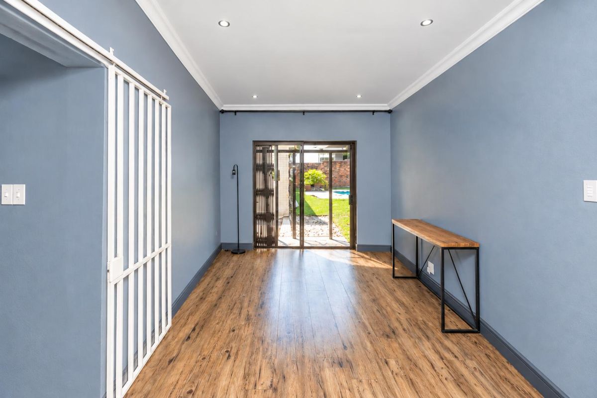 A bright, empty living area featuring wood-look laminate flooring, recessed lighting, and a sliding glass door providing direct access to the rear garden.