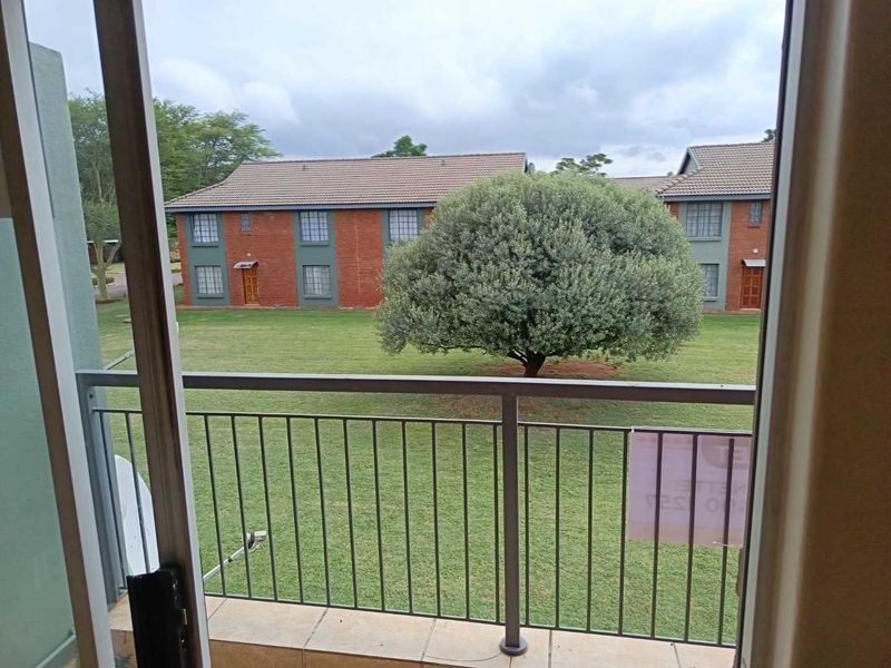 A balcony with a metal balustrade and tiled flooring, offering a view over the complex garden and neighboring apartment buildings.