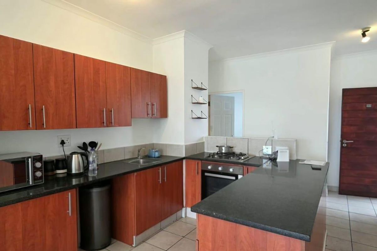 Functional kitchen featuring wood-finish cabinetry, granite countertops, a gas hob, and built-in oven, with tiled flooring and direct access to the entrance area.