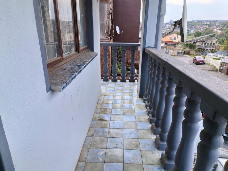 An outdoor balcony featuring a balustrade and tiled flooring, offering an elevated view of the surrounding neighborhood.