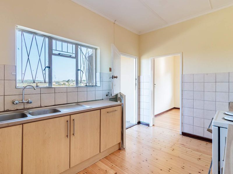A functional kitchen featuring timber flooring, laminate cabinetry, a stainless steel double sink, and tiled splashbacks, offering a clean and practical workspace.