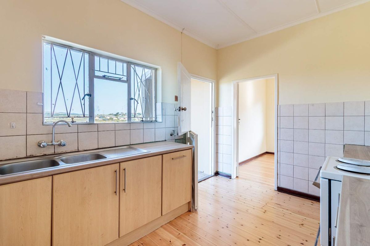 A functional kitchen featuring timber flooring, laminate cabinetry, a stainless steel double sink, and tiled splashbacks, offering a clean and practical workspace.