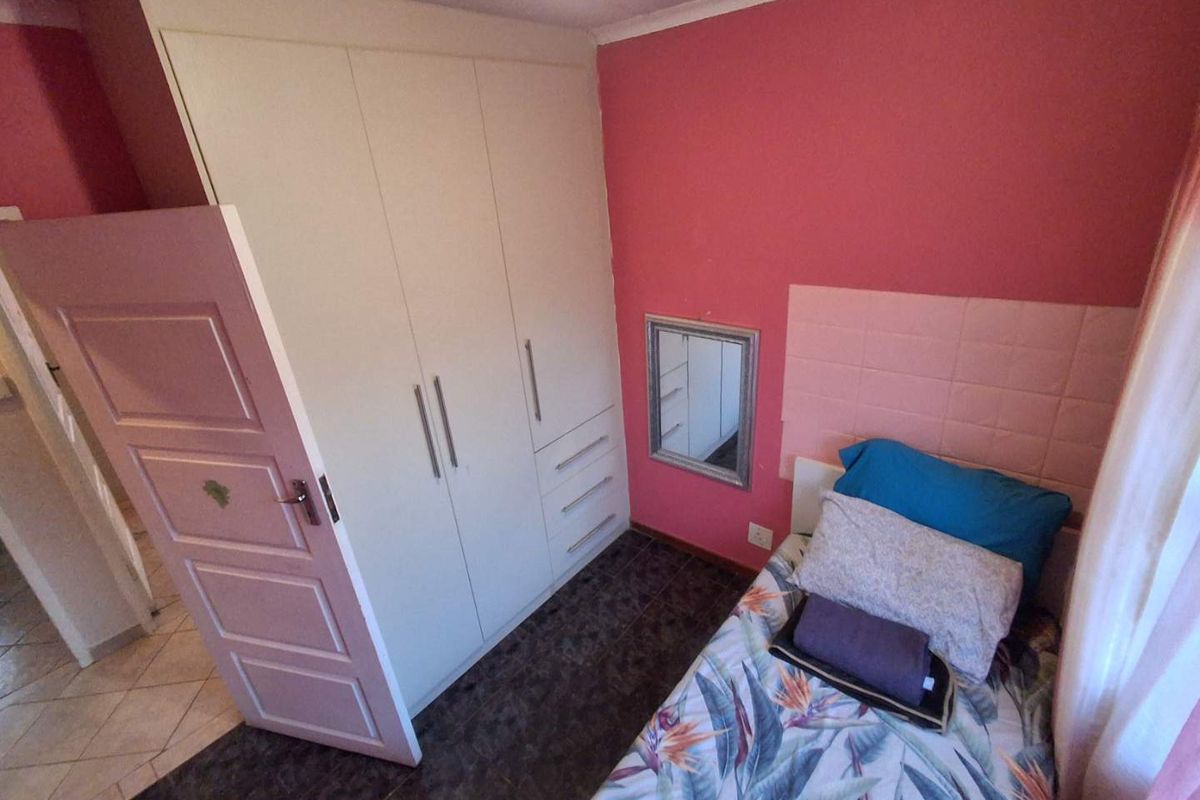 A compact bedroom featuring built-in cabinetry, tiled flooring, and a pink accent wall.