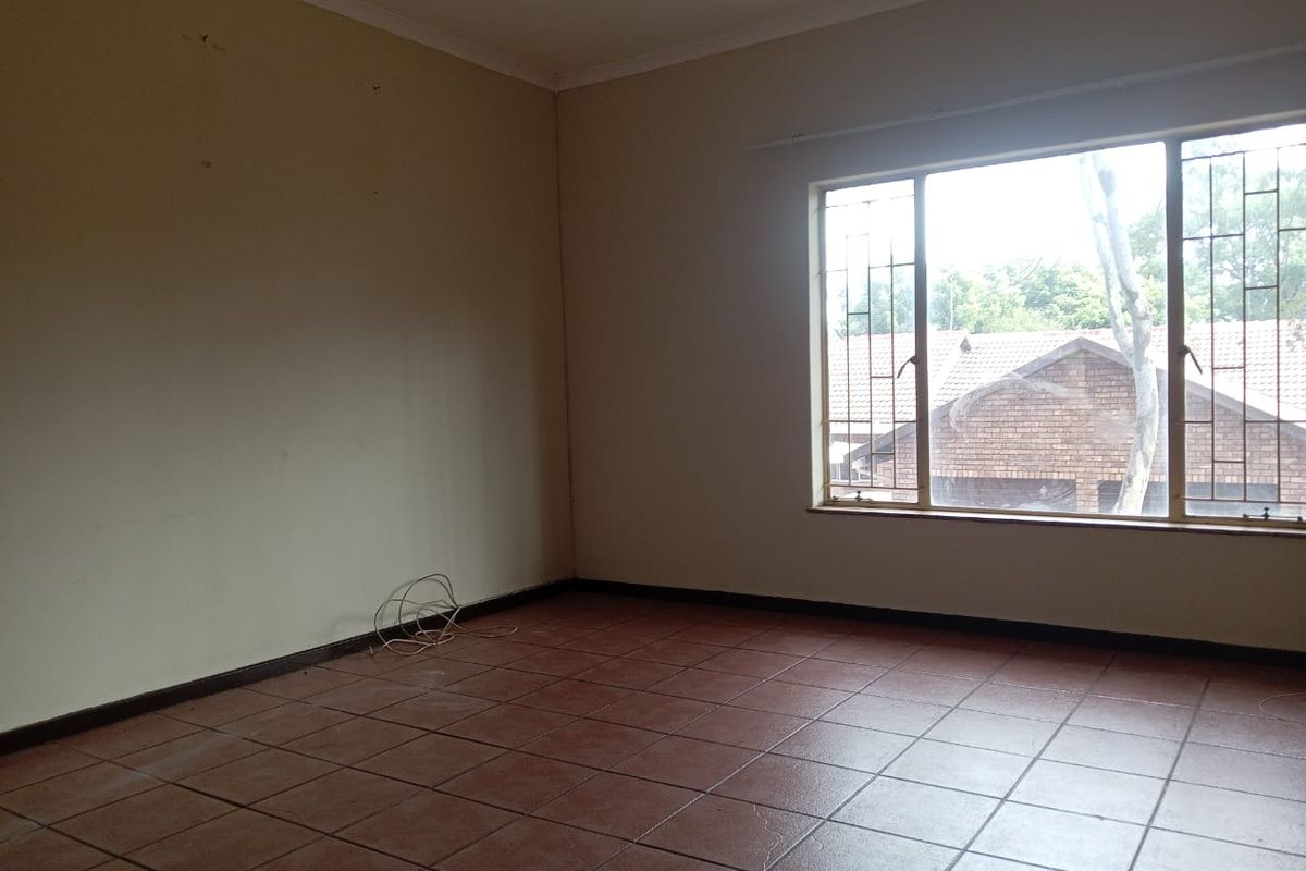 An empty living room featuring tiled flooring and a large window with security bars, offering a blank canvas for potential renovation.