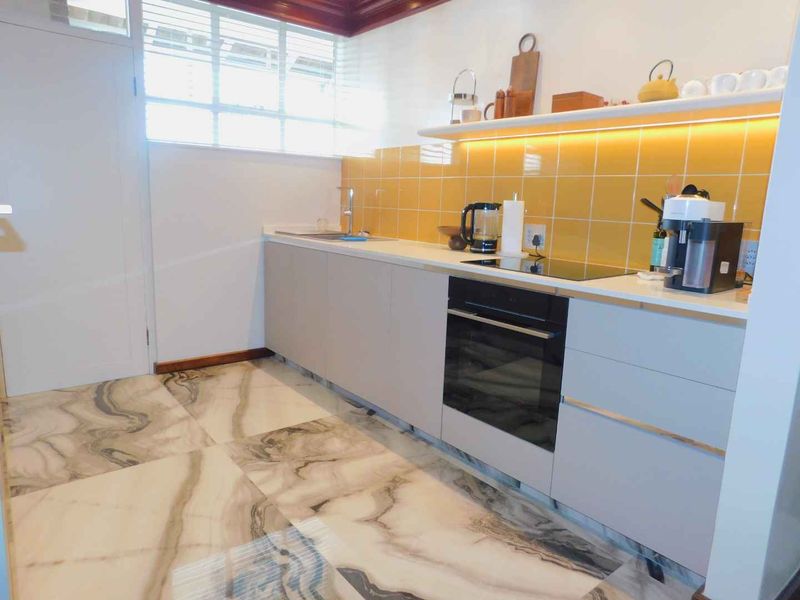 Modern kitchen featuring sleek cabinetry, stone countertops, integrated oven, electric hob, and stylish marble-effect flooring with warm under-cabinet lighting.