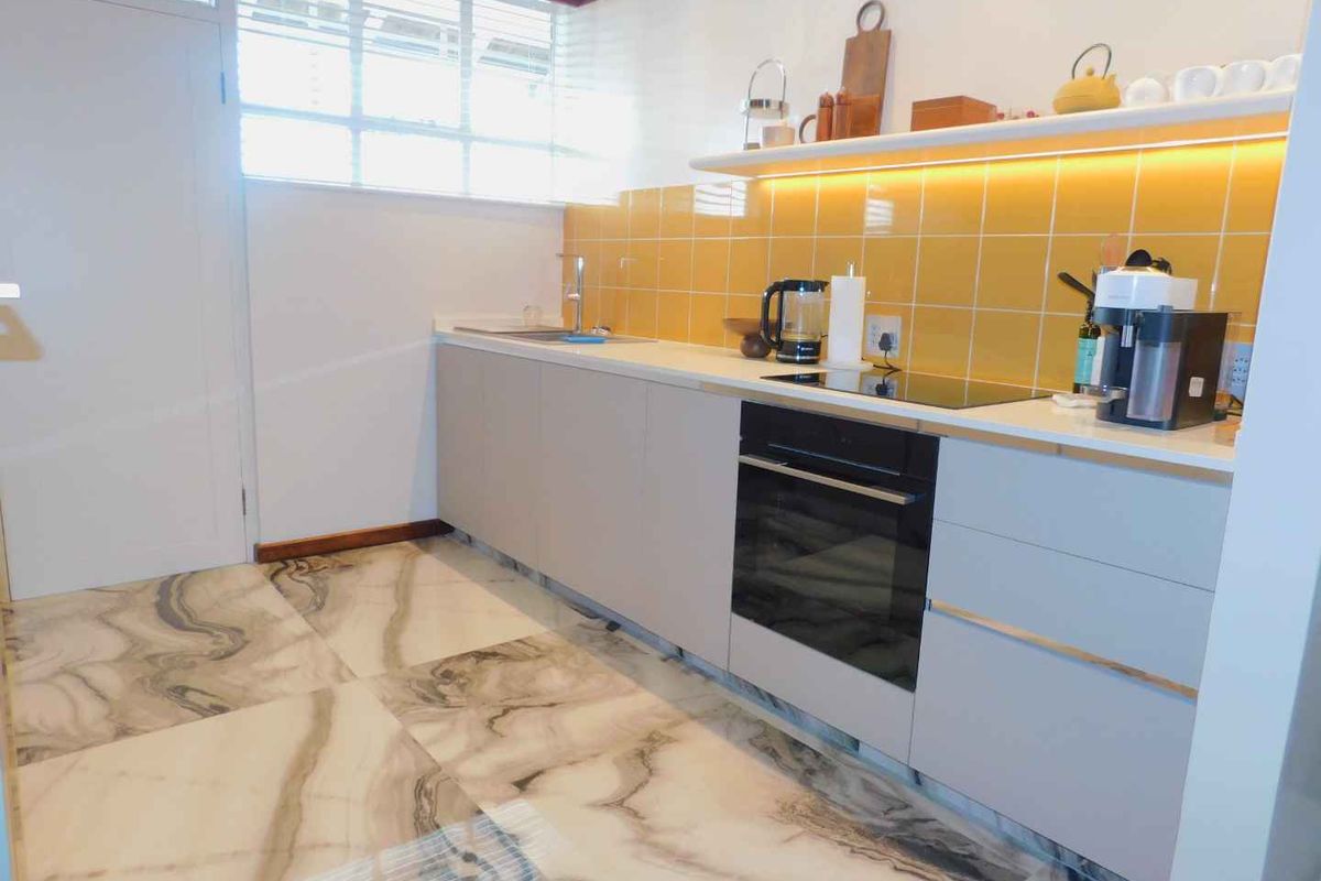 Modern kitchen featuring sleek cabinetry, stone countertops, integrated oven, electric hob, and stylish marble-effect flooring with warm under-cabinet lighting.