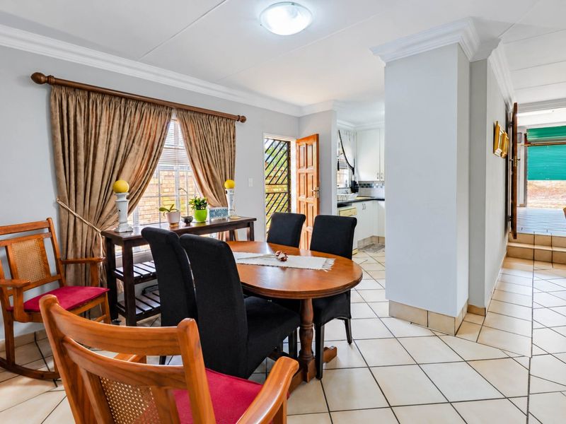 Open plan dining area featuring tiled flooring and ceiling cornices, with a view through to the adjacent kitchen and exterior access.