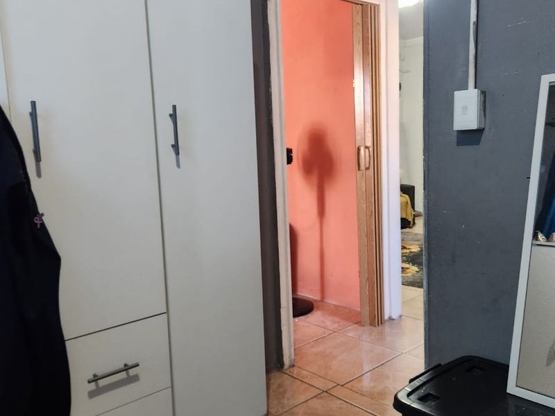 A bedroom interior featuring tiled flooring, a built-in wardrobe, and a folding door leading to an adjacent room with exposed electrical conduit.