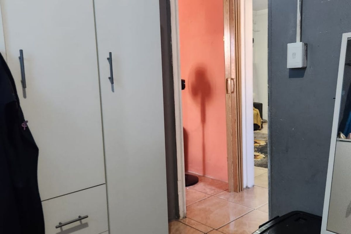 A bedroom interior featuring tiled flooring, a built-in wardrobe, and a folding door leading to an adjacent room with exposed electrical conduit.