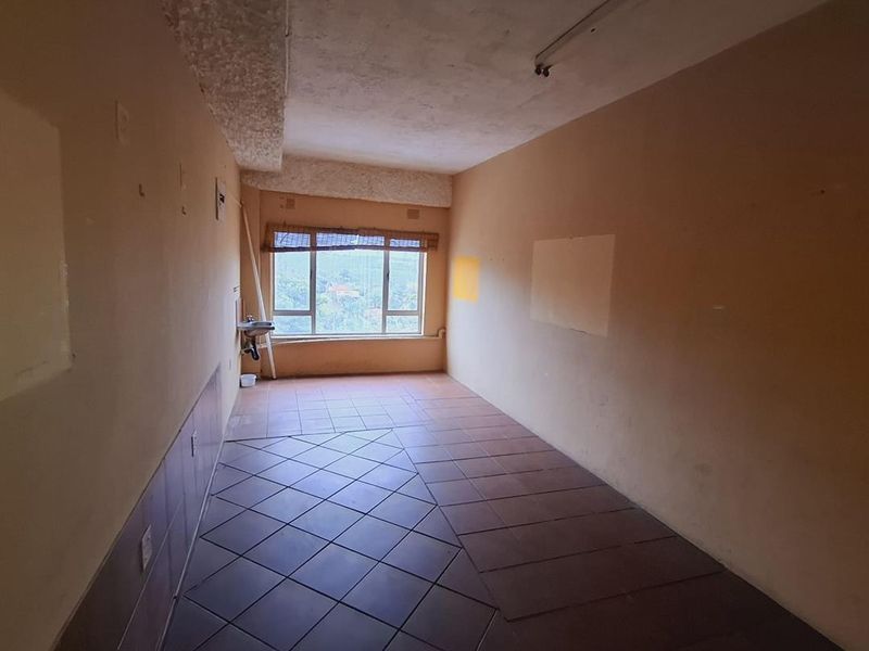 An empty, vacant office space featuring tiled flooring, a small wall-mounted basin, and a large window providing natural light.