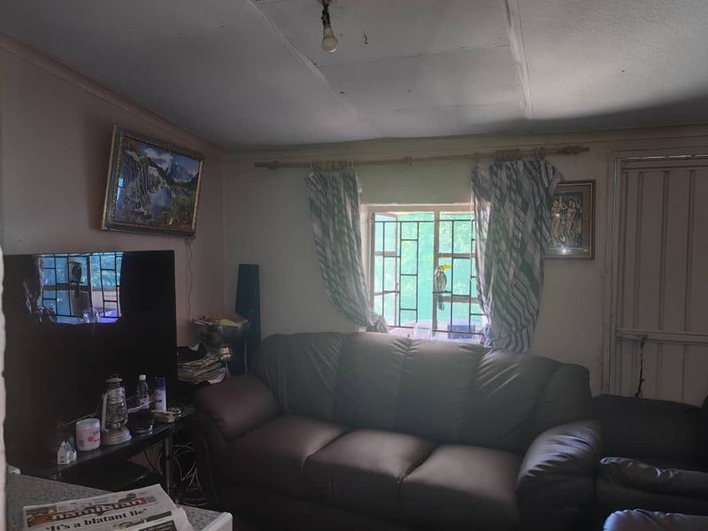 A living room featuring security bars on the window and ceiling tiles, requiring cosmetic updates to improve the overall aesthetic and condition.