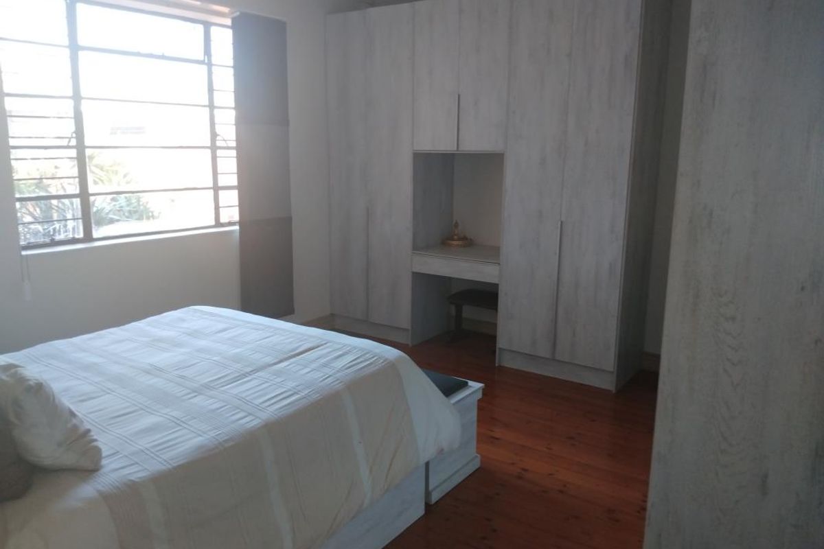 A bedroom featuring timber flooring, a large steel-framed window, and extensive built-in cupboards with an integrated vanity station.