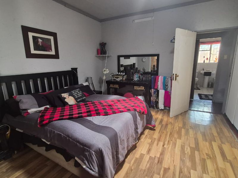 A bedroom featuring laminate flooring and built-in cupboards, with an adjoining bathroom visible through the doorway.
