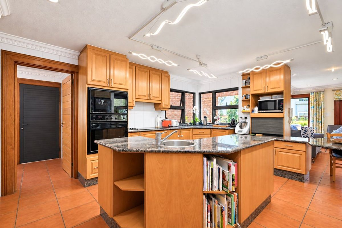 Spacious kitchen featuring wooden cabinetry, granite countertops, a central island with a sink, and built-in appliances, finished with durable tiled flooring.