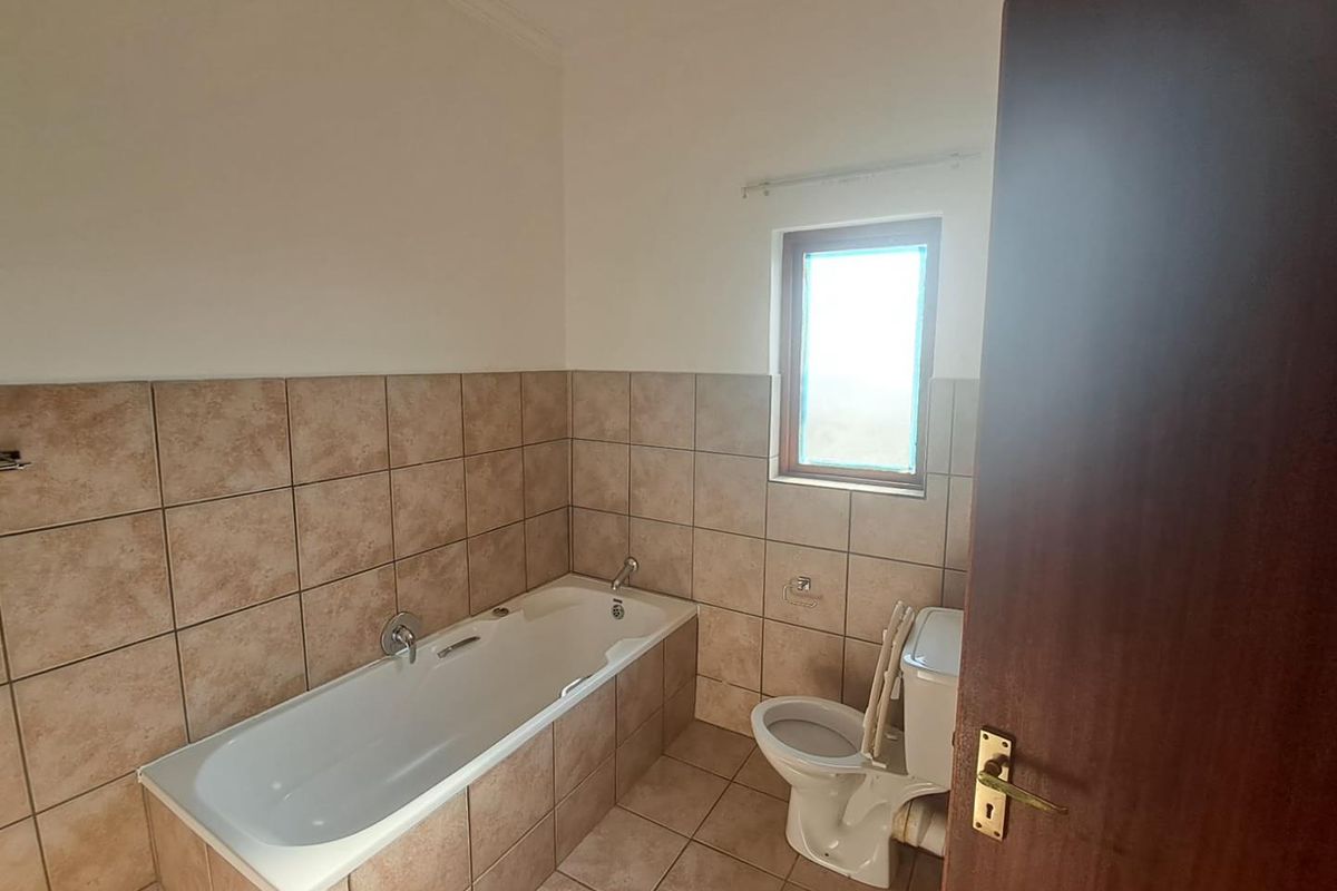 A functional bathroom featuring a built-in bathtub, toilet, and neutral wall and floor tiling, offering a clean space ready for potential updates.