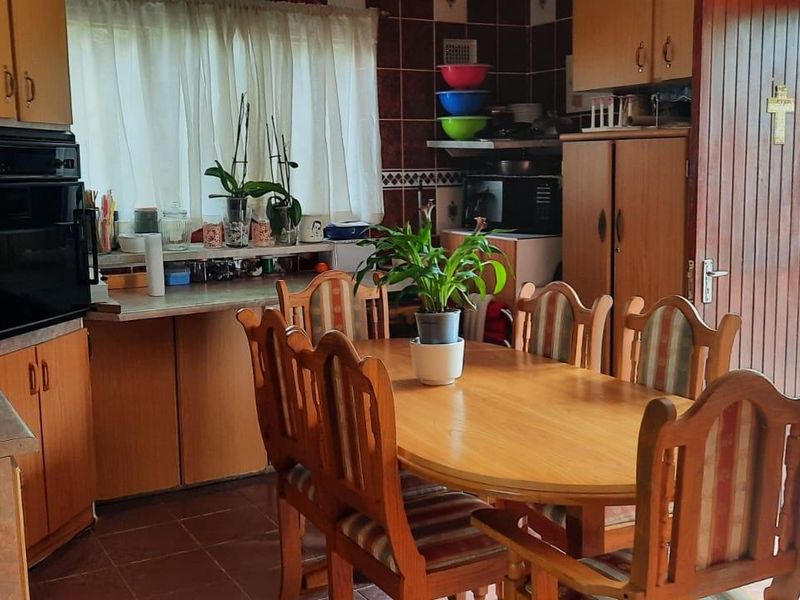 Open plan kitchen and dining area featuring dated wooden cabinetry, tiled backsplash, and direct access to an outdoor area through a security gate.