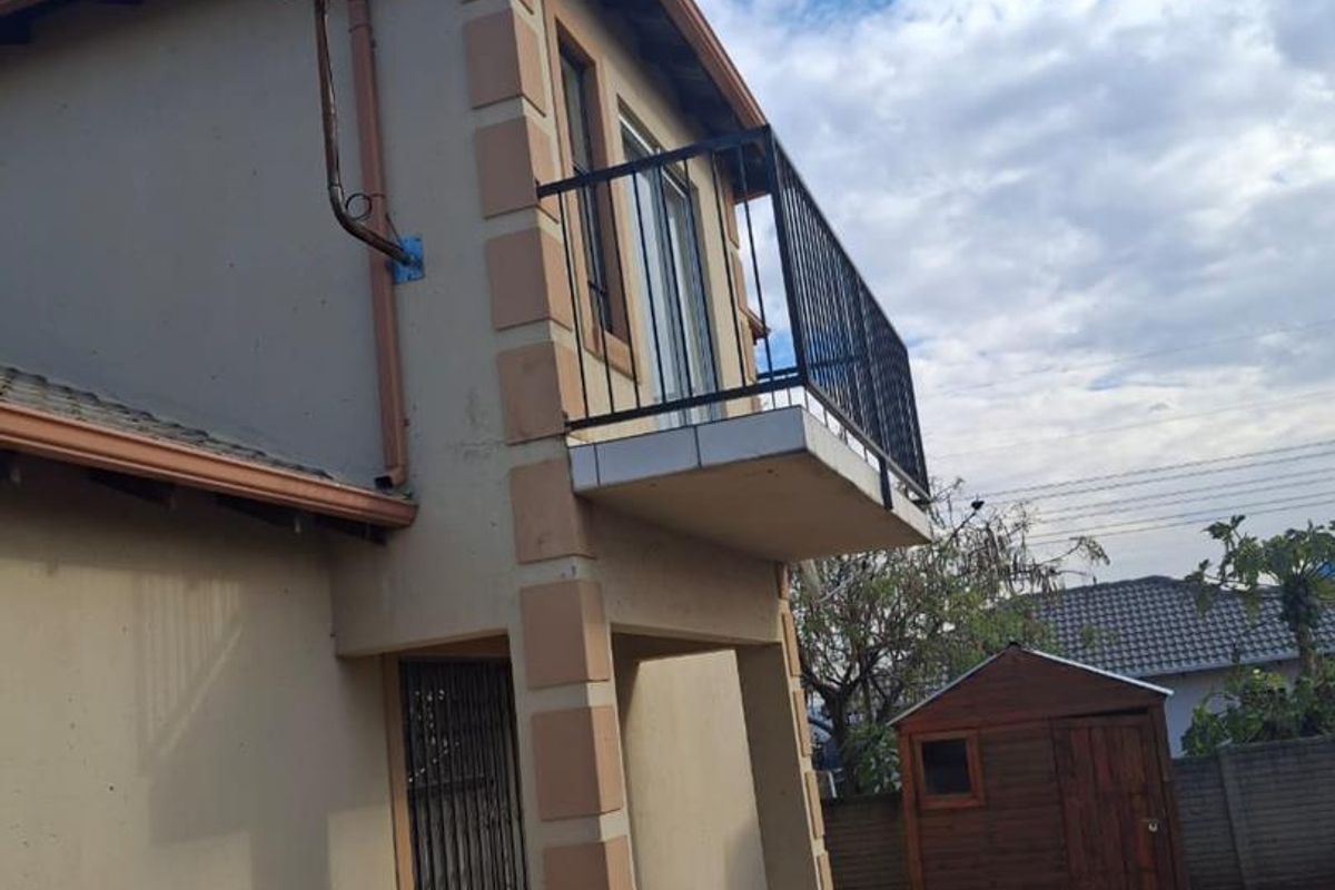 Rear view of the property featuring a balcony with metal railing, a tiled patio area, paved walkway, and a detached wooden garden shed.
