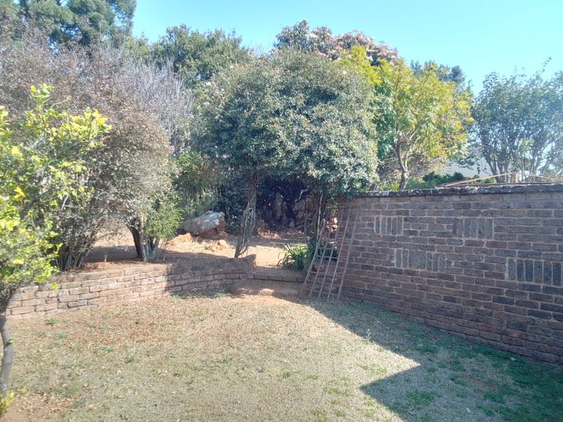 A private garden area featuring a brick boundary wall, mature trees, and stone steps leading to a rear section of the property.