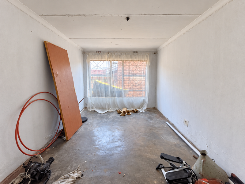 An empty bedroom featuring concrete flooring and a window with security bars, requiring cosmetic updates and floor finishing.
