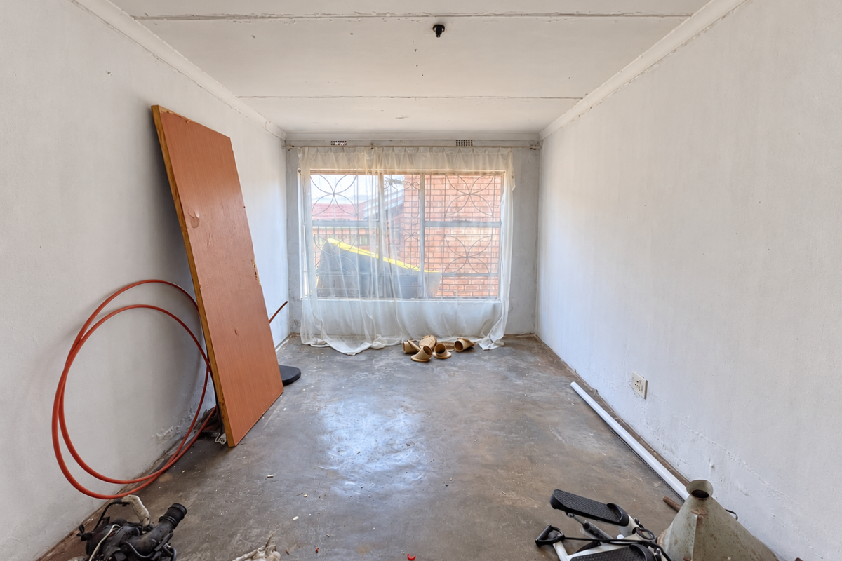 An empty bedroom featuring concrete flooring and a window with security bars, requiring cosmetic updates and floor finishing.