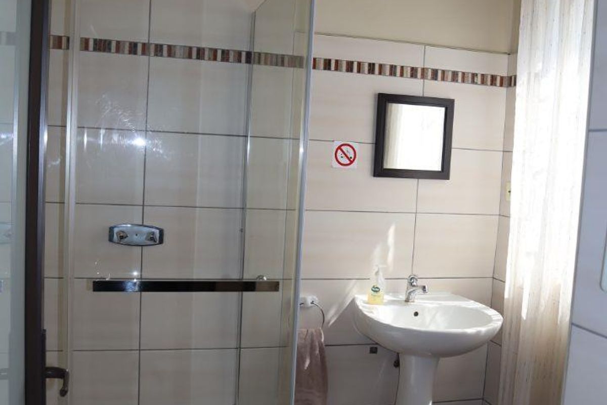 A functional bathroom featuring a glass-enclosed shower, pedestal basin, and tiled flooring, offering a clean and practical layout.