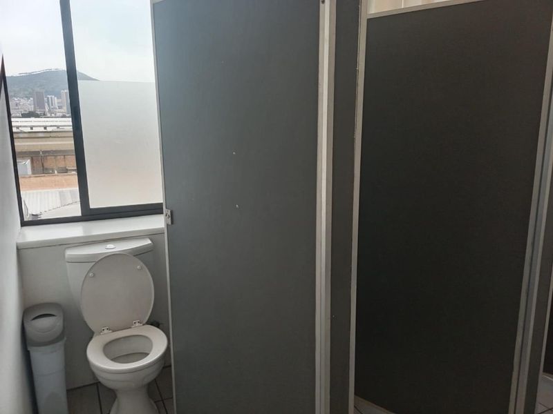 A functional office bathroom featuring partition walls and a window with city views.