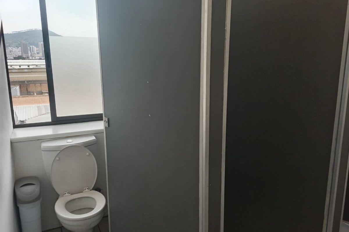 A functional office bathroom featuring partition walls and a window with city views.