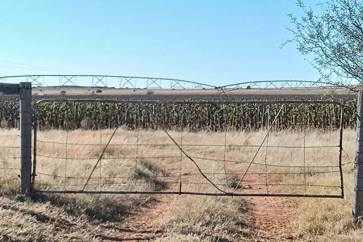 View of a farm field featuring a central pivot irrigation system and a wire-fenced perimeter with a metal gate.