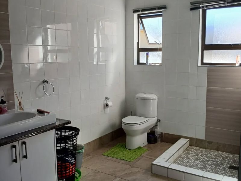 A clean, functional bathroom featuring a vanity cabinet, toilet, and a tiled shower base with neutral wall and floor tiling.
