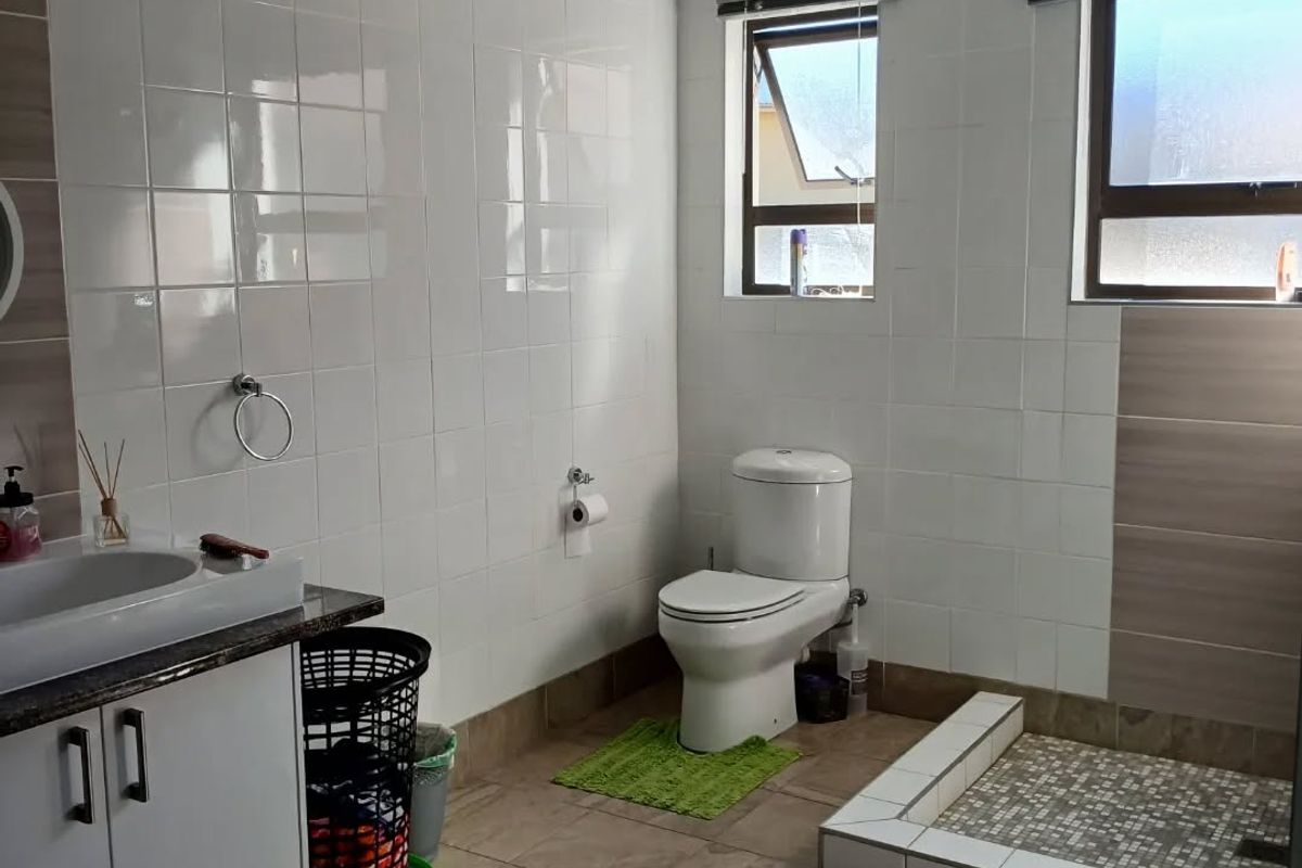 A clean, functional bathroom featuring a vanity cabinet, toilet, and a tiled shower base with neutral wall and floor tiling.