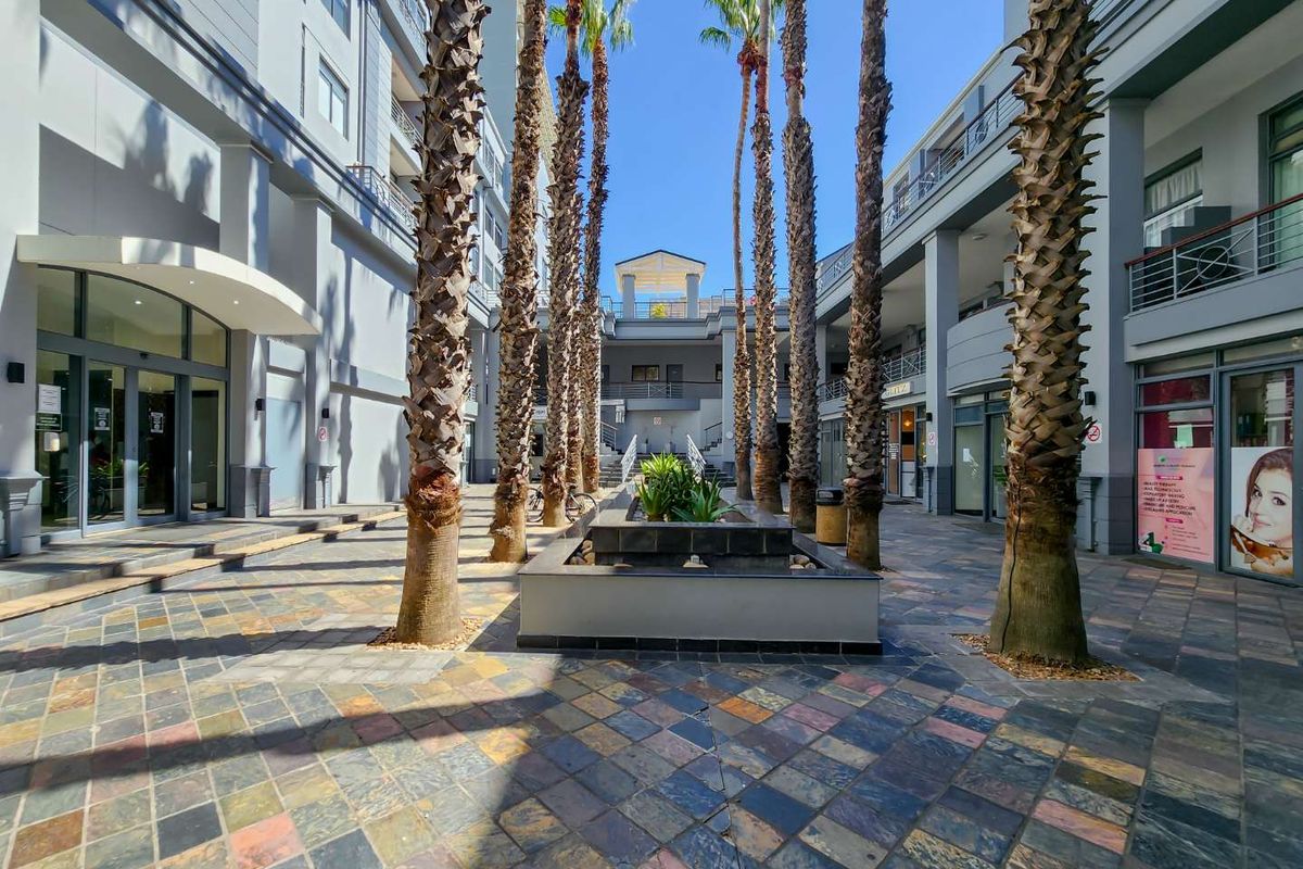 A well-maintained apartment complex courtyard featuring paved flooring, mature palm trees, and a central raised planter box.