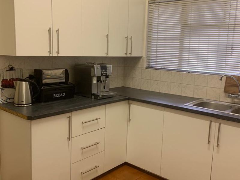 A functional kitchen featuring white cabinetry, dark laminate countertops, a stainless steel sink, and tiled flooring.